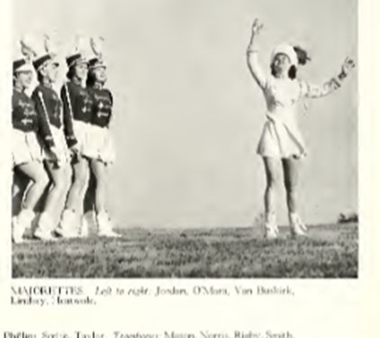 A black and white photo from 1952 shows four marching women to the left holding majorette batons. To the right is a marcher in white looking ready to catch a baton that is out of range of the photograph.