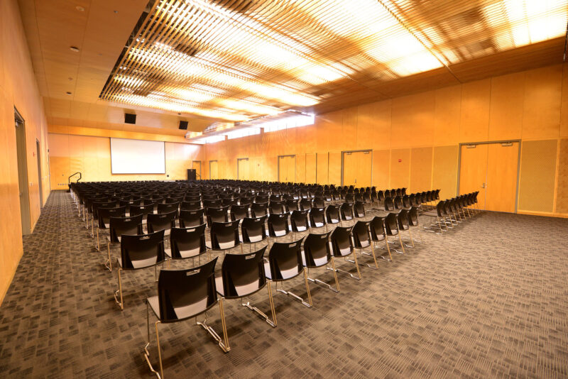 Kendall Cram Lecture Hall is a large room with carpeted floors and light wooden walls. With lots of light overhead.